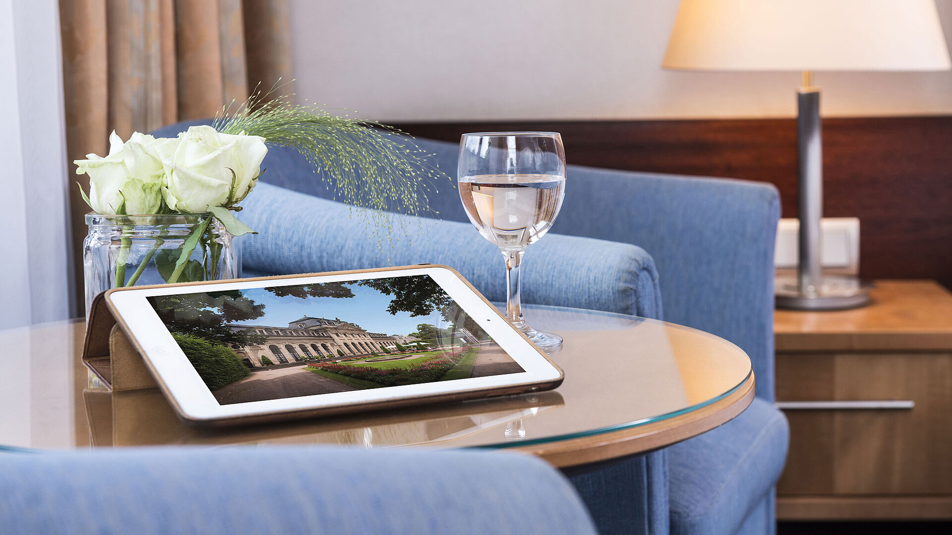 Cozy seating area at Maritim Hotel Fulda with tablet, glass of water, and white roses on a glass table.